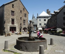 Visitors gather around a historic fountain in Besse en Chandesse, enjoying the warm sunshine and