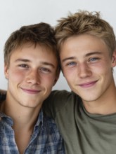 Two smiling young men in casual clothes pose in a friendly manner against a wall, symbolising