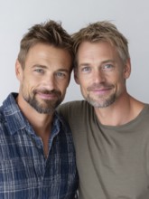 Two smiling men in casual clothes pose friendly on a wall, symbolic image for same-sex
