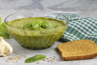 Basil pesto in a glass bowl with bread, garlic and chequered cloth