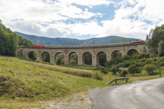 Train crossing Adlitzgraben viaduct, cloudy sky and green hills, Semmering railway, Semmering,