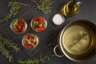 Cooking pot, herbs and jars filled with hot peppers on a dark background