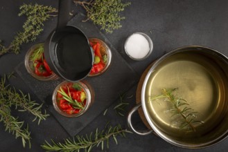 Cooking pot with vinegar, jars with chilli peppers and herbs on a dark background