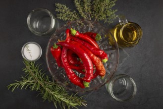 Several red peppers, chilli peppers alongside oil, salt, herbs and empty jars