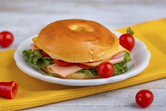 A filled bagel on a plate, decorated with tomatoes on a yellow cloth