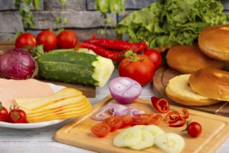 Bagels alongside sausage, cheese and fresh vegetables such as tomatoes, lettuce, cucumber and