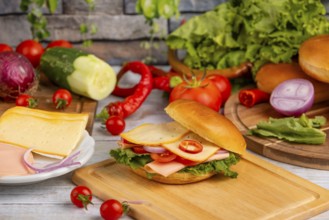 A bagel topped with cheese, sausage, salad and vegetables, surrounded by fresh ingredients