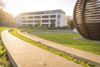 Wooden sphere-shaped structure next to modern residential complex in sun-drenched park, small town