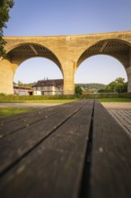 Massive stone bridge arches in the sunshine above a wooden bench, small town of Perle Nagold, Black
