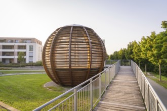Wooden spherical structure in front of modern residential building at sunset in urban park, small