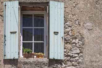 A window with blue shutters in a rustic house wall with flowering potted plants, Provence, France