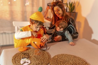 Two young brothers wearing halloween costumes are playing at a table with their mother, enjoying