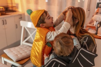 Two brothers, dressed up in halloween costumes, applying makeup on their mother's face, creating a