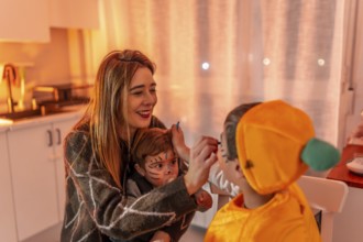 Happy family preparing for halloween party, mother applying makeup on children's faces, creating