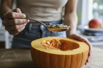 Woman scooping pumpkin seeds from a fresh pumpkin in the kitchen. Preparing pumpkin seeds for