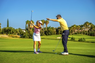 Experienced golf instructor guiding a female golfer on a sunny day, providing tips for a perfect