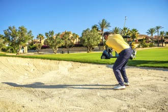 Golfer concentrating on hitting ball out of sand trap on a beautiful sunny day, with golf cart in