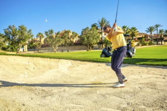 Professional golfer hitting a ball out of a sand trap on a sunny day, showcasing skill and