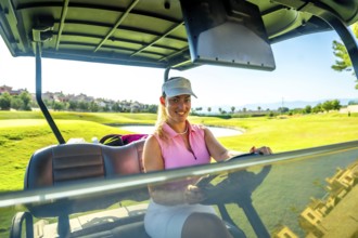 Smiling woman enjoying a sunny day while driving a golf cart through a picturesque golf course,