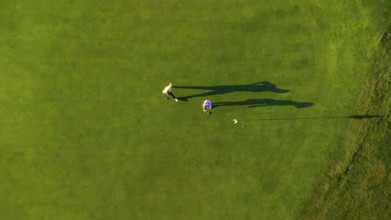 Two golfers are putting on a vibrant green golf course, seen from an aerial perspective, creating