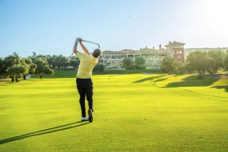 Golfer swings his club on a beautiful, sunny day, aiming for the green with a luxurious resort in
