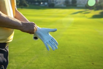 Golfer putting on a white golf glove, getting ready for an exciting game on a lush, vibrant green