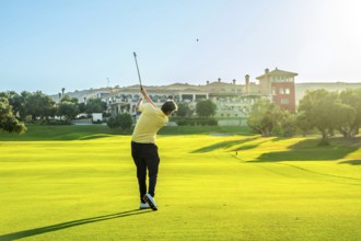 Golfer hitting a shot on a beautiful, sunny golf course with a luxury resort in the background