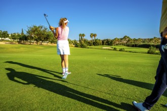 Woman golfer swinging her club on a sunny golf course, preparing to hit the ball towards the hole
