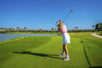 Woman golfer focusing intently on putting the ball on a sunny day, with a picturesque lake creating