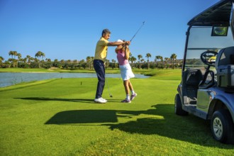 Golf instructor guiding female golfer on a sunny course, improving her swing technique near a golf