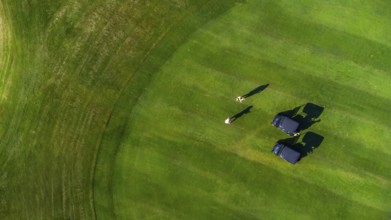 Aerial view of two golfers playing on a perfectly manicured green golf course, enjoying a sunny day