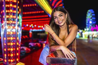 Happy young woman enjoying the vibrant atmosphere of a funfair, posing near colorful attractions at