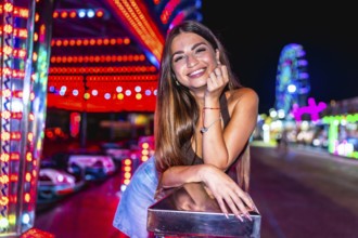 Happy woman enjoying night at amusement park, leaning on railing with colorful bumper cars and