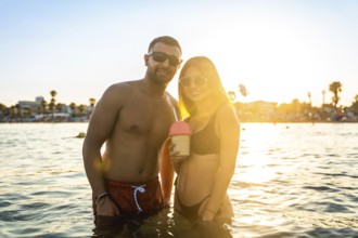 Young couple enjoying a refreshing drink in the sea at sunset, creating a romantic and carefree