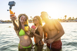Group of cheerful young friends taking a selfie with action camera while enjoying cocktails in the