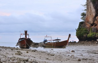 Two traditional thai longtail boats sit peacefully on the shore of railay beach, krabi, thailand,