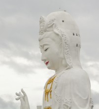 Majestic white guan yin statue, a prominent buddhist figure, stands tall against a cloudy sky in