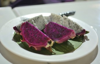Vibrant slices of red and white dragon fruit are presented on a banana leaf atop a white plate,