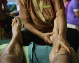 Close up of a thai masseuse performing a relaxing leg massage on a tourist, showcasing the