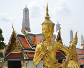 Golden kinnara statue praying with hands joined in a traditional thai greeting, inside the wat phra