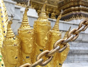 Golden garuda statues adorned with intricate metal chains stand prominently in the foreground,