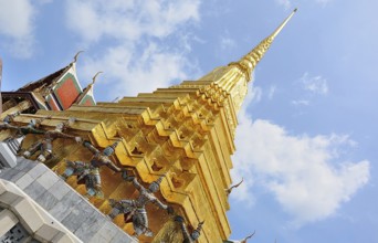 Golden chedi reaching for a bright blue sky, supported by decorative figures, within the majestic