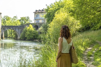 Woman enjoying the scenic view of the gave d'oloron river and the historic bridge during a summer