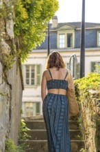 Tourist with tote bag walking up stone stairs in the historic village of salies de bearn, france,