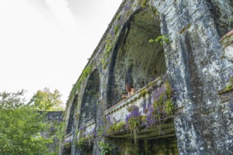 Tourist admiring the landscape from a balcony of an ancient aqueduct covered in vegetation in