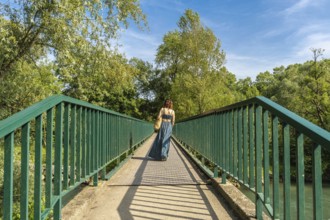 Woman walking away on a pedestrian bridge over gave d'oloron river, visiting sauveterre de bearn in
