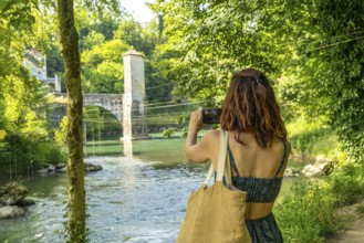 Young woman photographing a medieval bridge over gave d'oloron river in sauveterre de bearn, a