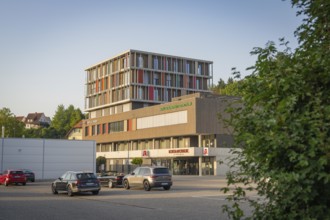 Modern building structure next to a car park with several cars in the sunlight, Nagold, district of