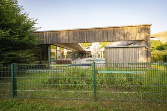 Modern building with wooden wall and garden, surrounded by a green fence in sunshine, Nagold,
