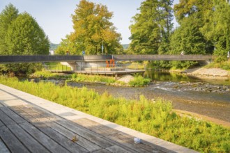 River landscape with bridge, surrounded by green trees and a wooden footbridge along the path,